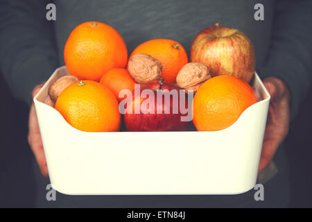 Close-up of a man holding a bowl of apples, oranges and  walnuts Stock Photo