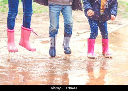 Low section of three children in wellington boots jumping in a puddle Stock Photo