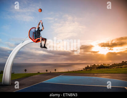 Young man sitting in a basketball hoop in a park, Los Angeles, California, USA Stock Photo