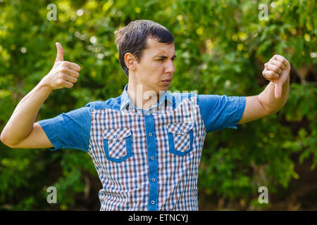 Man outdoors thumbs up thumbs down on a green background leaves Stock Photo
