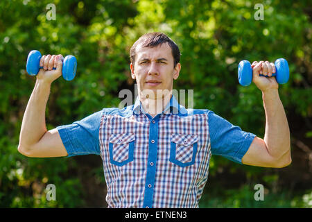 The man in the street holding a plastic dumbbells sport on a blu Stock Photo