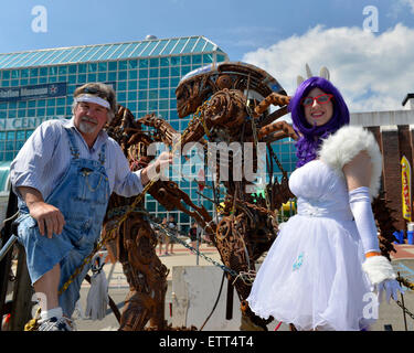 Garden City, New York, USA. 14th June 2015. HALE STORM of Freeport, the sculpture, and LAURA GIUNTA, of Levittown, cosplaying as Rarity from My Little Pony, pose, each holding a chain of The Predator and The Alien sculpture by artist Storm, outdoors at Eternal Con, the Long Island Comic Con, at the Cradle of Aviation museum. The sculptor created the life-size metal artwork from automotive and motorcycle parts. Credit:  Ann E Parry/Alamy Live News Stock Photo