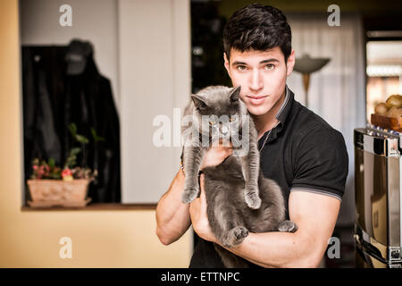 Handsome Young Animal-Lover Man Inside the House, Hugging his Gray Domestic Cat Pet. Stock Photo