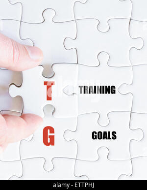 Hand of a business man completing the puzzle with the last missing piece.Concept image of Business Acronym TG as Training Goals Stock Photo
