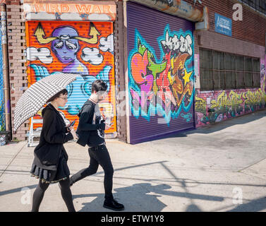 Visitors walk past work at the Welling Court Mural Project in the Astoria neighborhood of Queens in New York on Saturday, June 13, 2015. The annual neighborhood event decorates walls in this industrial part of Astoria. The project is crowd-funded and emerging street artists work side by side with established stars.  (© Richard B. Levine) Stock Photo