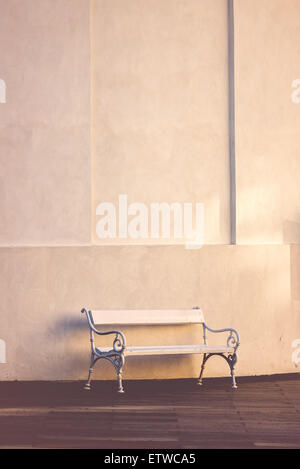 Vintage White Wooden Bench Against Tall Concrete Wall, Retro Toned Cross Process Image Stock Photo