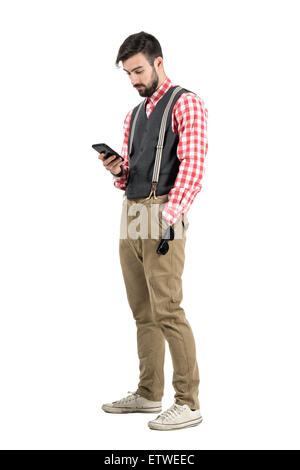 Relaxed young man in retro clothes typing message on smartphone. Full body length portrait isolated over white studio background Stock Photo