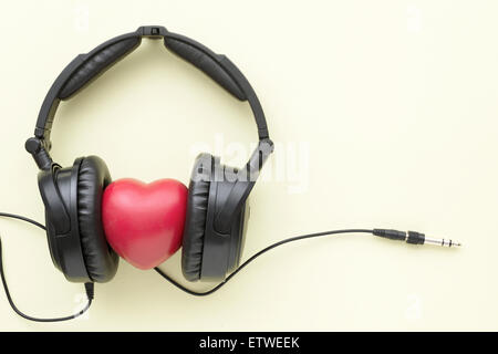 black headphones with red heart, wires and socket on light yellow background Stock Photo