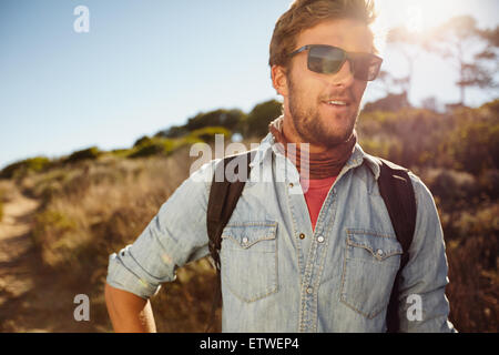 Portrait of happy young man hiking in countryside. Caucasian male model with backpack hiking on sunny day. Summer vacation in co Stock Photo