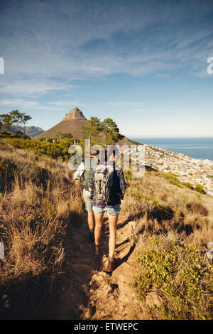 Rear view of couple walking through country path on mountain. Young man and woman hiker hiking in nature. Trekking together summ Stock Photo