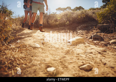 Low angle view of two people hiking along a dirt trail in the wilderness.  Couple of hikers walking on country path. Stock Photo