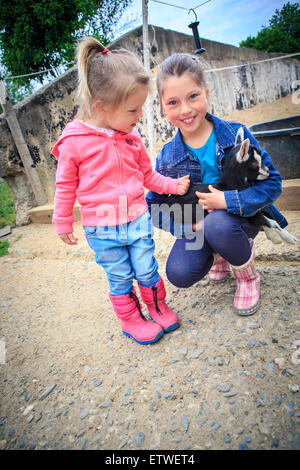 little girls with a goat kid in front of the farm Stock Photo