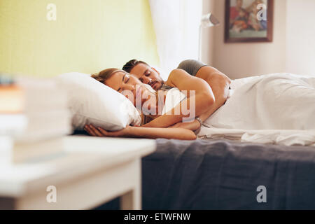 Young adult couple sleeping peacefully on the bed in bedroom. Young man embracing woman while lying asleep in bed. Stock Photo