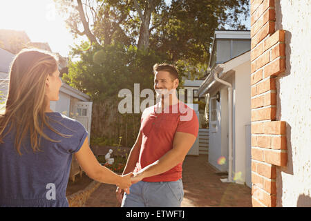 Happy young man holding hand of his girlfriend and walking around their house. Loving young couple outdoors in their backyard on Stock Photo