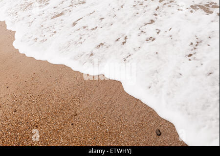 Low tide ripples wave patterns in shallow frothy bubbly sea water as it draining water runs off sandy shingle beach Stock Photo
