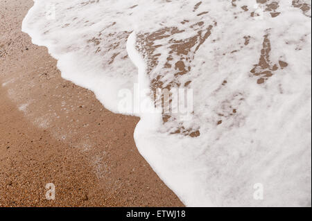 Low tide ripples wave patterns in shallow frothy bubbly sea water as it draining water runs off sandy shingle beach Stock Photo