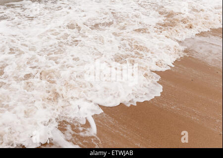 Low tide ripples wave patterns in shallow frothy bubbly sea water as it draining water runs off sandy shingle beach Stock Photo