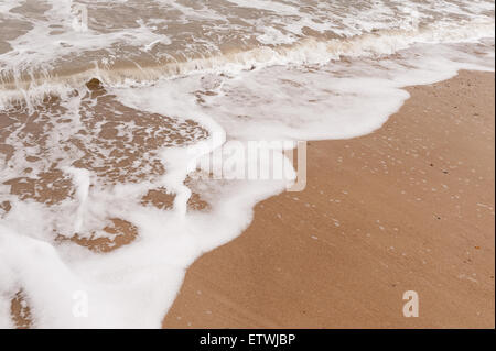 Low tide ripples wave patterns in shallow frothy bubbly sea water as it draining water runs off sandy shingle beach Stock Photo