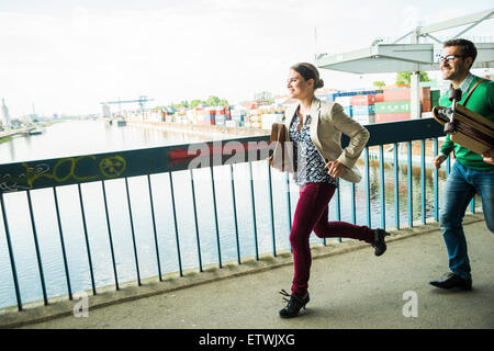 Young woman and man with skateboard running on bridge Stock Photo