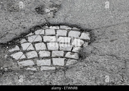 Pothole with old gray stone pavement on damaged urban asphalt road Stock Photo