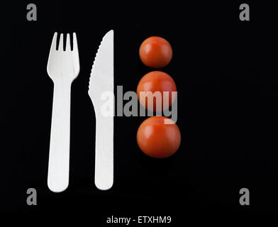 Fork, knife and three cherry tomatoes - culinary composition, isolated on black Stock Photo