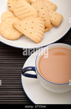 Close up of a cup of tea with milk on a saucer and a plate of shortbread biscuits biscuit from above Stock Photo