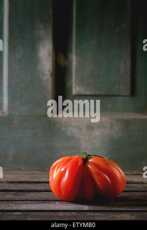 One big red tomato RAF over old wooden table. Dark rustic atmosphere Stock Photo