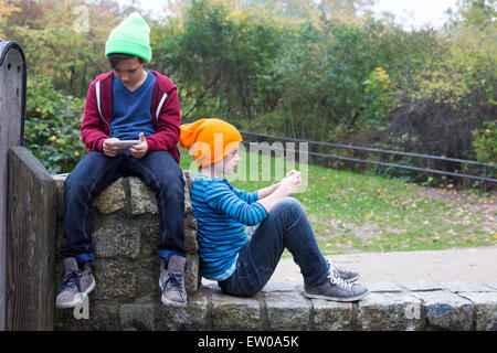 two young boys sitting outside and playing with their phones Stock Photo