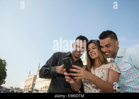 Three young Latin people using cell phone outdoors Stock Photo