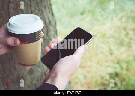 Man in a park holding a smartphone and a cup of coffee Stock Photo