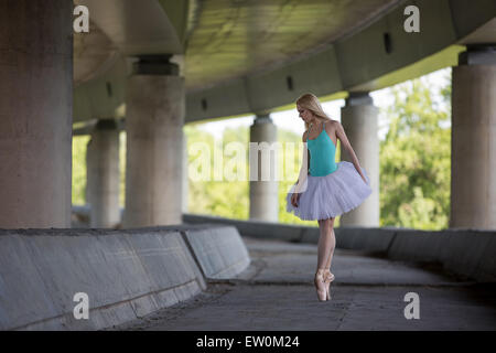 Graceful ballerina doing dance exercises on a concrete bridge Stock Photo