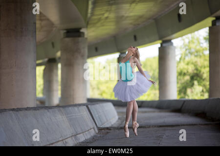 Graceful ballerina doing dance exercises on a concrete bridge Stock Photo