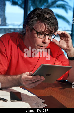 Man in holiday setting surprised by detail screen information on his iPad Air tablet computer with iPhone 6 smartphone nearby Stock Photo