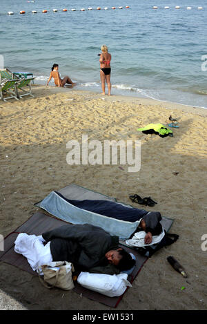 Two vagrants sleeping rough on the beach in Pattaya Thailand while two tourists are taking photographs Stock Photo