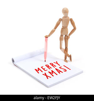 Wooden mannequin writing in a scrapbook - Merry xmas Stock Photo