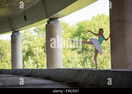 Graceful ballerina doing dance exercises on a concrete bridge Stock Photo