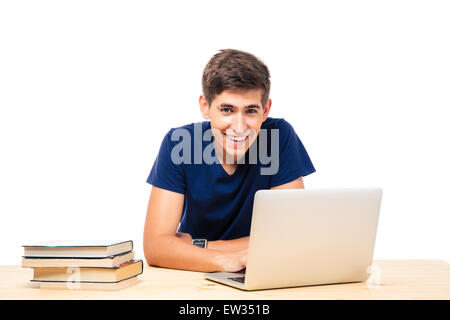 Happy male student sitting at the table and using laptop isolated on a white background Stock Photo