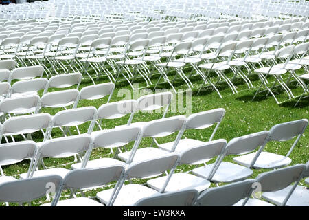 Rows and rows of white foldup chairs set out facing one way as an auditorium on grass for a concert Stock Photo