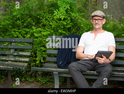 man sitting on a bench in a park with tablet in his hand Stock Photo