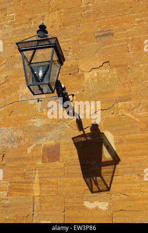 Lantern with crisp shadow,  against the orange ironstone of the stable block at Althorp House, home of Earl Spencer Stock Photo