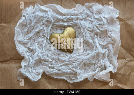 Shattered, gold painted heart on white tissue paper inscribed with the word LOVE.Brown paper background Stock Photo