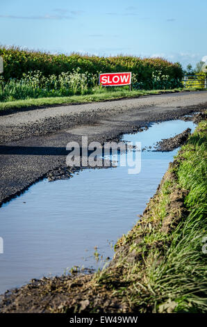 Water filled pot hole on a country road with a 'SLOW' sign in the background Stock Photo