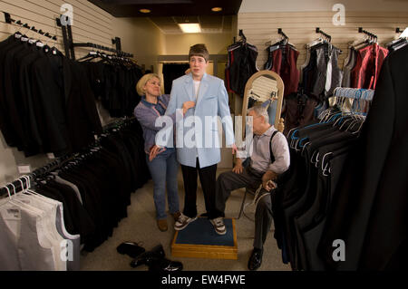 Teenage boy looking unhappy is being fitted with blue suit jacket while overbearing mother and tailor assist Madison Wiscon Stock Photo