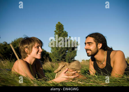 Man and woman lying down in grass while together holding a tree Maine. Stock Photo