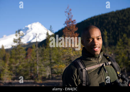 African American man Cupid Alexander stands with binoculars in forest near Mt. Hood in the Cascade Mountains Oregon. Stock Photo
