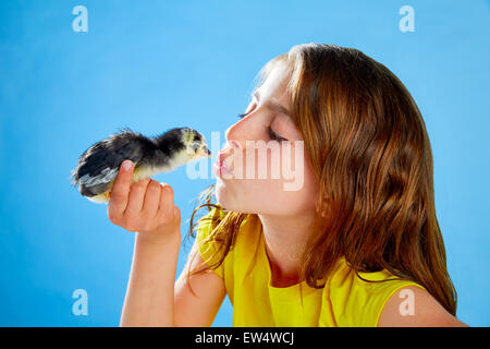 Kid girl kissing chick playing on table with blue background Stock Photo