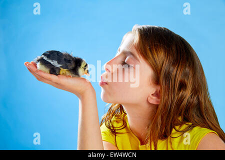 Kid girl kissing chick playing on table with blue background Stock Photo