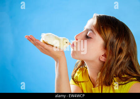 Kid girl kissing yellow chick playing on table with blue background Stock Photo