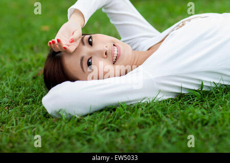 Young woman lying on the lawn with hands on head Stock Photo