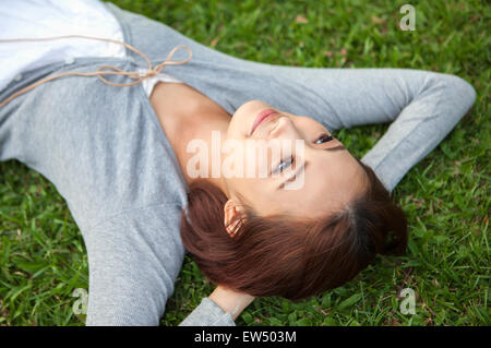 Young woman lying on the lawn and looking away with hands behind head Stock Photo